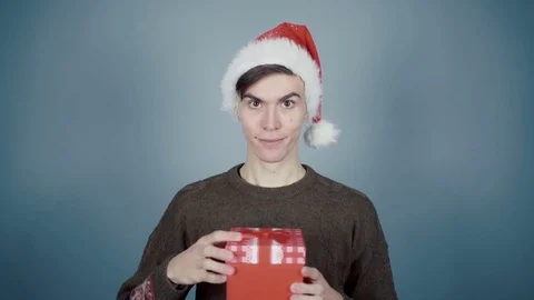 Young man in Santa hat opening a gift box with a surprise inside seeing coffee Stock Footage 70223623