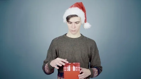 Young man in Santa hat opening a gift box with a surprise inside seeing little Stock Footage 70223655