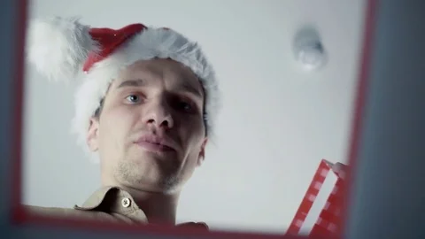 Young man in Santa hat opening a gift box with a surprise inside seeing Video stock 70223787