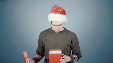 Young man in Santa hat opening a gift box with a surprise pulls out long Video stock 70223868