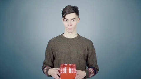 Young man in Santa hat opening a gift box with a surprise inside looking Stock Footage 70223874