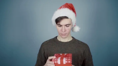 Young man in Santa hat opening a gift box with a surprise inside seeing burning Stock Footage 70223932