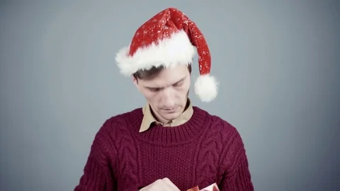 Young man in Santa hat opening a gift box and pulling out an ink pen Stock Footage 70261021
