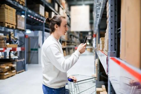 Young man scanning barcode on box with smartphone in furniture warehouse st.. Stock Photos