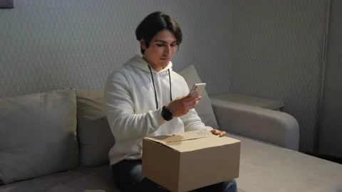 Young man scanning QR code on the parcel by mobile at home 스톡 동영상 173017480