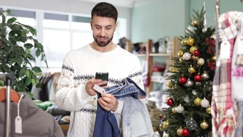 Young man scanning qr code of jeans in store Vídeo Stock 344775705