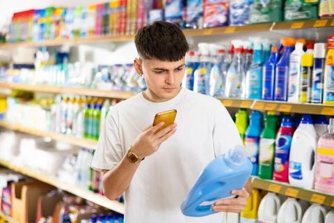 Young man scanning qr-code on bottle of laundry detergent in supermarket Stock Photos