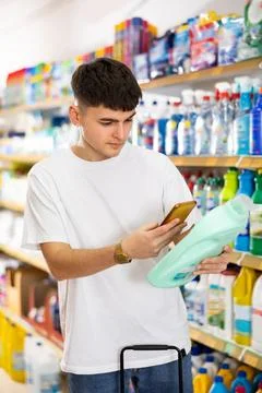 Young man scanning qr-code on bottle of laundry detergent in supermarket Stock Photos