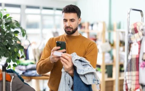 Young man scanning QR-code on jeans in clothing store Stock Photos