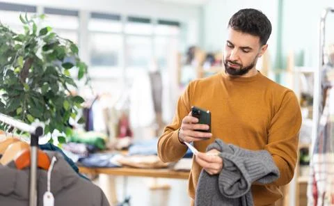 Young man scanning QR-code on sweater in clothing store Stock-Fotos