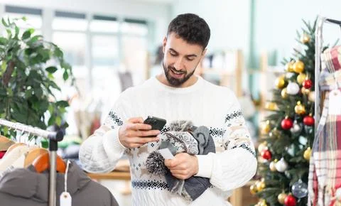 Young man scanning QR-code on hat in clothing store during Christmas Stock-Fotos