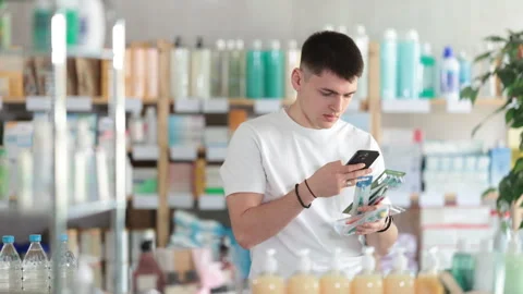 Young man scans the barcode of a toothbrush package in a pharmacy. Guy takes a Stock Footage 309524182