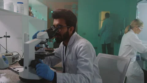 Young man scientist with glasses and protective gloves looking in the microscope Stock Footage 252138146