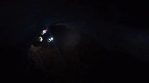 Young man scrambles out on all fours from narrow hole in cave with flashlight Stock Footage 80053589