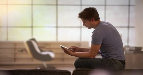 Young man scrolling on a tablet while sitting on a couch Stock Footage 78610031