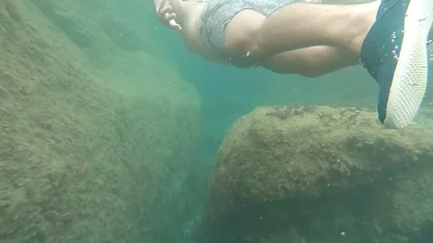 Young man scuba diving with fish in a rocky and calm area of the sea, slow mo Stock Footage 142007757
