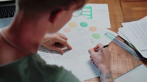 Young man searching through textbook and notes, writing on the laptop Stock-Footage 164371555