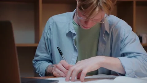 Young man searching through the textbook and writing notes, doing homework Stock Footage 164374074