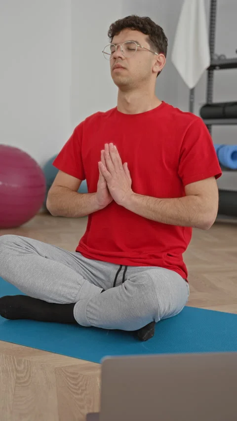 Young man seated cross legged on a yoga mat with hands in prayer pose and l.. Stock Footage 339196902