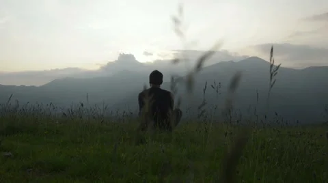 Young man seated on the grass is watching at panorama at sunset Stock-Footage 64516406