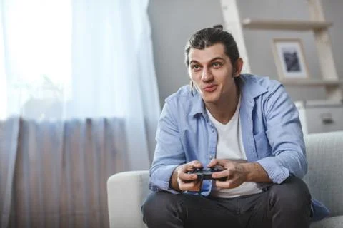 Young man seated on a sofa playing video games inside his room Stock Photos