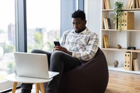 Young man seated using smartphone in modern cozy apartment interior 스톡 사진
