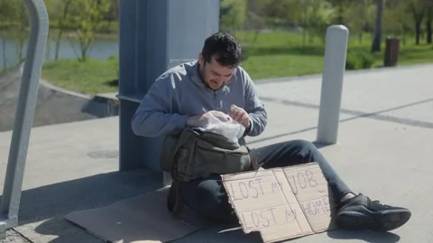 Young man seeks help while struggling with homelessness in urban park Stock Footage 307195948