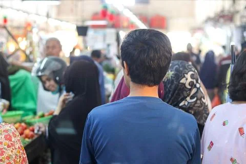 A young man is seen from behind queuing at a busy traditional market stall d Stock Photos