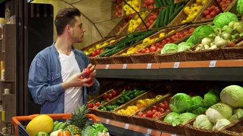 Young man selecting fresh tomatoes and cucumbers at the supermarket Stock-Footage 311989355