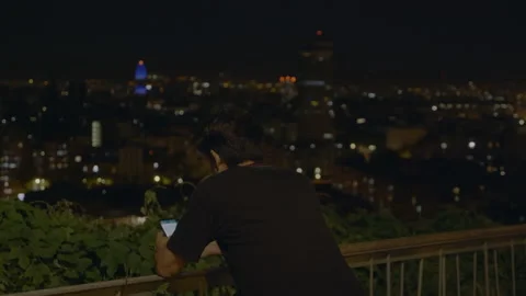 Young Man Sending a Message while Barcelona Skyline is watching, Night, 4K Vidéo 130901793