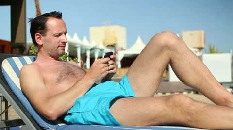 Young man sending sms while sunbathing by the pool HD Stock Footage 10888335