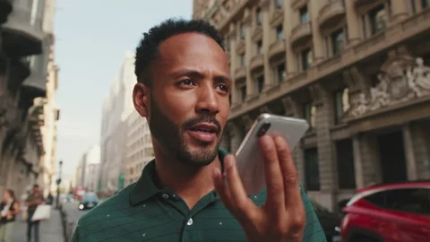 Young man sends voice message on cellphone while standing on the street next to Stock Footage 227096308