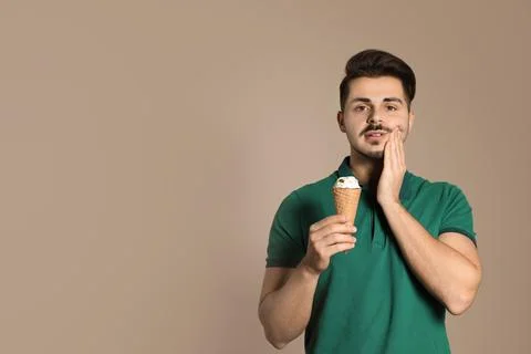 Young man with sensitive teeth and ice cream on color background. Space for t Stock Photos