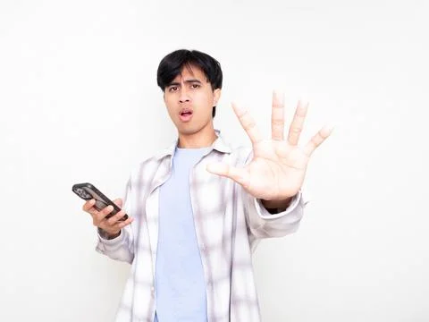 Young man with a serious expression holding a smartphone while raising his .. Stock Photos