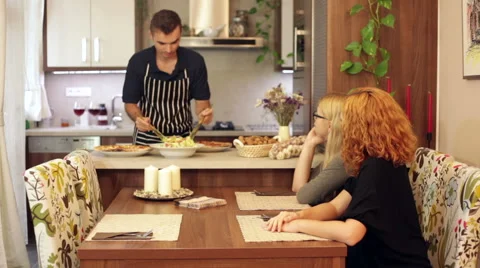 Young man serving vegetable salad for two women at home 库存影片 61460765