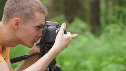 A young man sets the camera on a tripod and takes a picture. Stock Footage 92312031