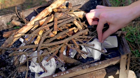 Young man sets fire to paper with match under clump of wooden branches for Stock Footage 276416703