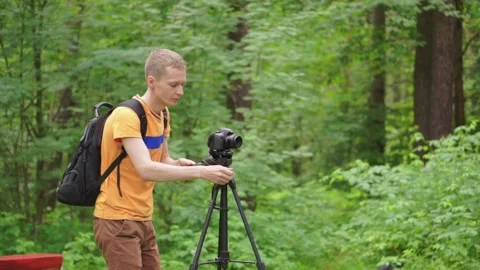 A young man sets up a tripod with a camera and takes a photo. Stock Footage 92312289