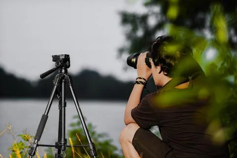 Young man setting up camera on the edge of the lake. Back view of male Sett.. Stock Photos