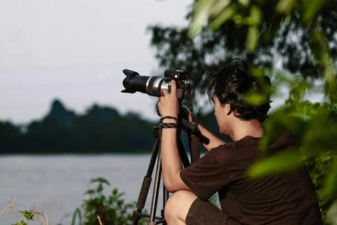Young man setting up camera on the edge of the lake. Back view of man Setti.. Stock Photos