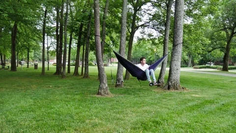 Young man setting up an eno hammock outside on trees Stock Footage 76224542