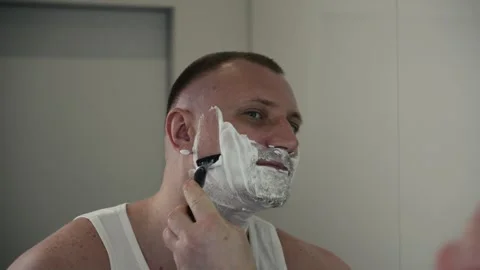 Young man shaving beard with manual razor in modern bathroom during morning Stock Footage 334630200