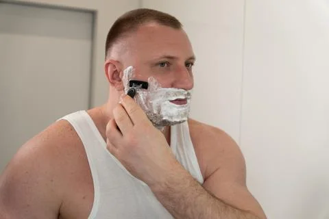 Young man shaving face with razor during morning grooming routine Фото