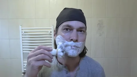 Young man shaving in front of a mirror with a classic razor Stock Footage 242284612