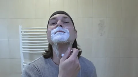 Young man shaving in front of a mirror with a classic razor Stock Footage 242287709