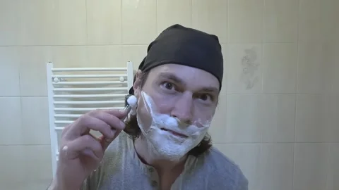 Young man shaving in front of a mirror with a classic razor Stock Footage 242288019