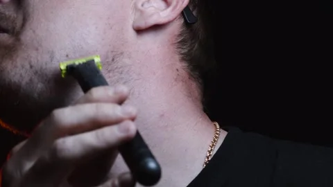 Young man shaving his face with a trimmer for shaving Video stock 308537871