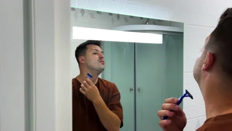 Young man is shaving his neck using a blue disposable razor in bathroom. Stock Footage 210722209