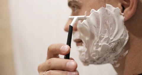 Young man is shaving using disposable razor in bathroom, closeup, side view. Stock Footage 137437840