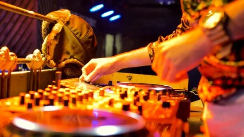 A young man in a shirt and clock rhythmically mixes music in a night club. Video stock 105963781